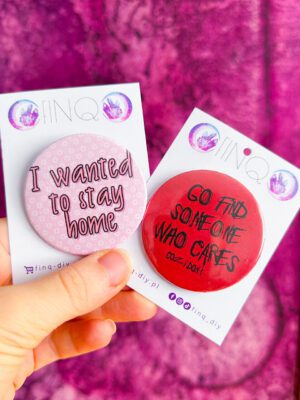 Dwie przypinki z napisami, jedna różowa i napisem "I wanted to stay home", druga czerwona i napisem "go and find someone who cares"