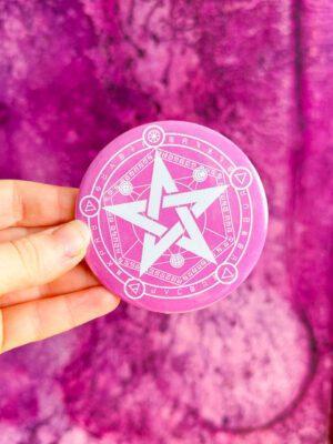 Bardzo duża przypinka typu button pin z pentagramem z symbolami alchemicznymi w kolorze różowo-białym.