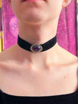 Welurowa obróżka o szerokości 25 mm, z zamocowanym po środku fioletowym ametystem w ozdobnej oprawie. Zaprezentowana na modelce.