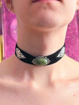 Czarny choker aksamitka z zielonym kamieniem (agat indyjski) w ozdobnej oprawie. Po bokach znajdują się dekoracyjne elementy. Zaprezentowany na modelce. Gotycka biżuteria witchy, royal, romantic goth.