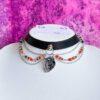 Czarny choker z ekoskóry z anatomicznym sercem, stalowymi łańcuszkami oraz czerwonymi i czarnymi koralikami w stylu gotyckim.